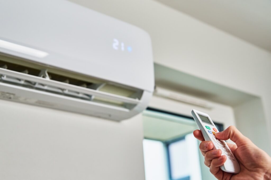 An indoor air conditioning unit, displaying a temperature of 21, is being controlled by a person's hand holding the remote.