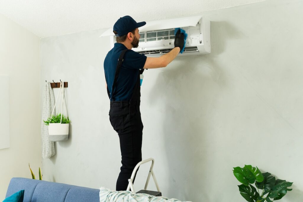 Technician performing maintenance on mini split air conditioning system, cleaning filters and vents with detergent and sponge how to clean ac filter