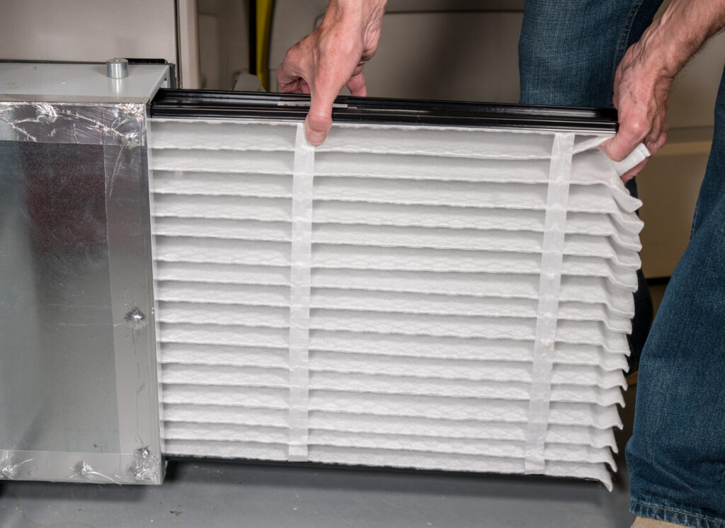 furnace filter replacement Senior caucasian man changing a folded air filter in the HVAC furnace system in basement of home