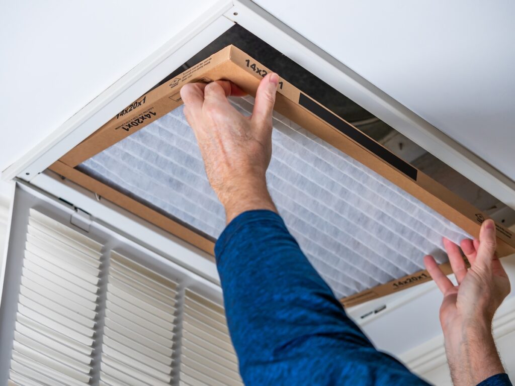 hvac duct installation Man replacing dirty HVAC air filter in ceiling vent. Home air duct system maintenance for clean air.