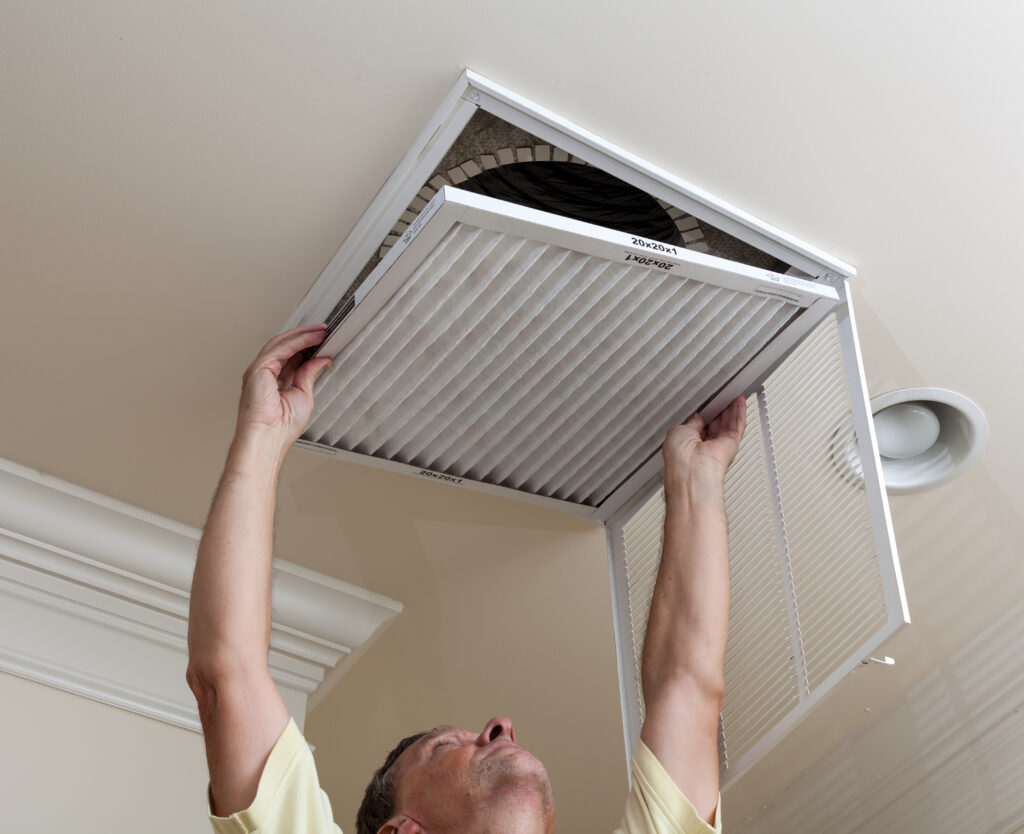 how to maintain heating and air conditioning Senior male reaching up to open filter holder for air conditioning filter in ceiling
