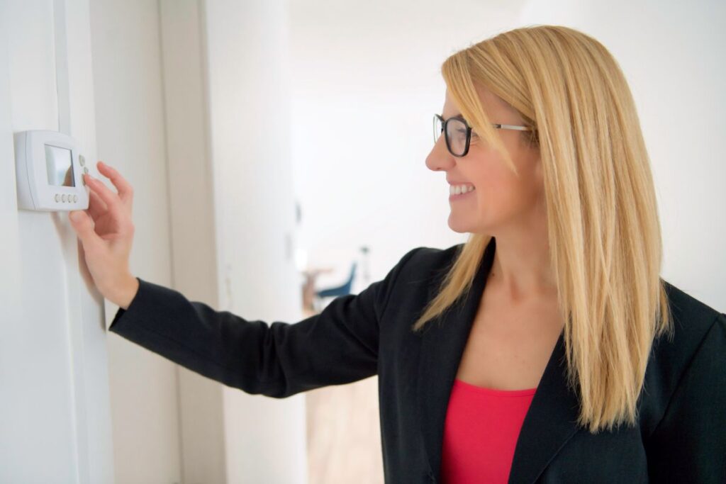 energy saving thermostat smiling business woman adjusting thermostat on white wall inside commercial building