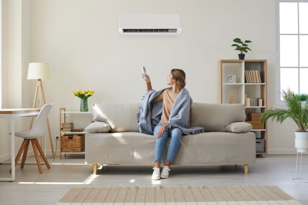 young woman controlling new hvac system cost sitting on nice grey coach inside big house with white walls desk small shelves